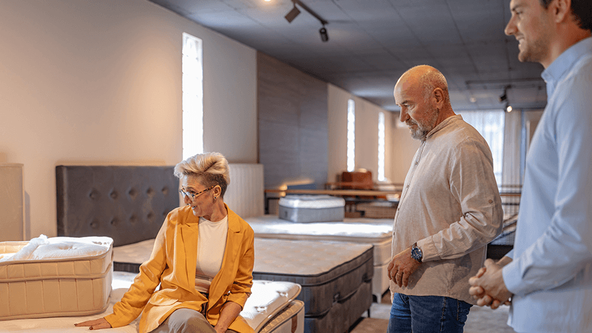 older woman on mattress, older man and younger salesman look on