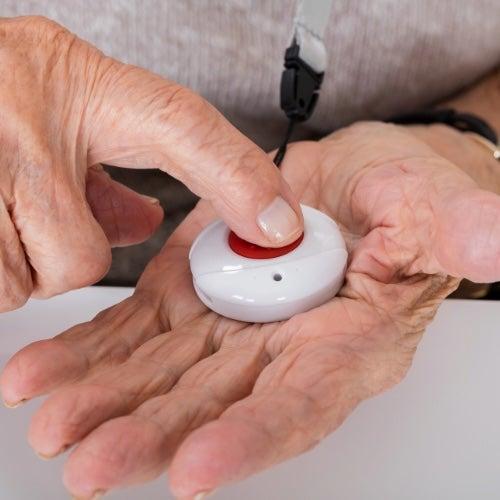A medical alert button in the palm of a person’s hand as they press the button with the other hand