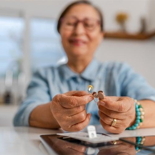 A woman sitting at a table and holding hearing aids