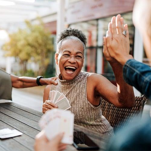 A woman playing cards laughs and high-fives the person sitting next to her.