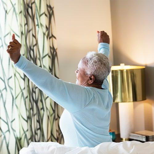 A woman stretches at the edge of her bed.