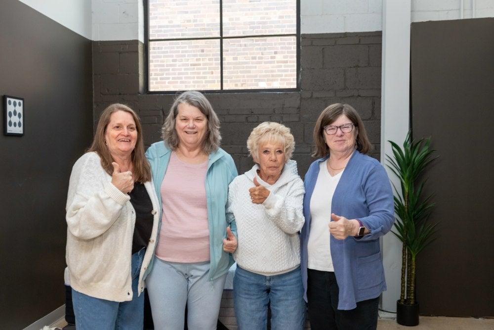 Group of older women smile while looking into the camera and giving a thumbs up