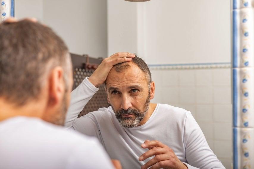 A man looks at his hair in the mirror