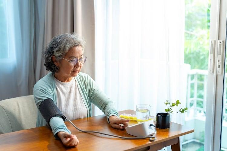 A woman sitting at a table using a home blood pressure monitor