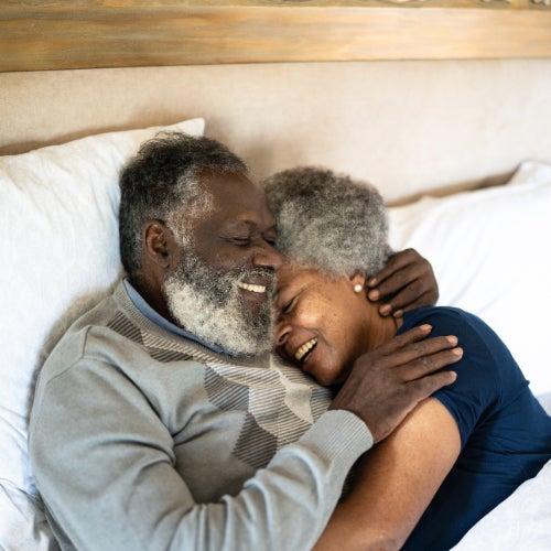 A man and a woman holding each other in bed and smiling