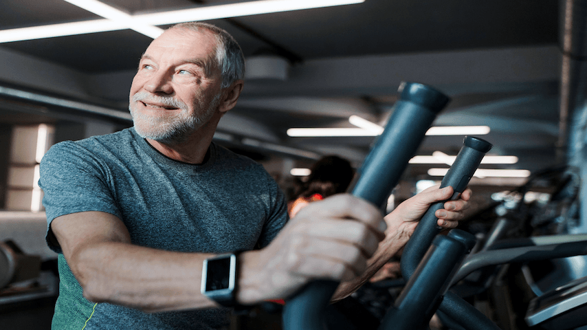 Older white man on an elliptical machine at the gym wearing a smartwatch