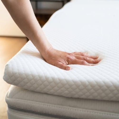A hand pressing down into a mattress topper on a bed
