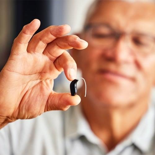 A man holds a hearing aid between his finger and thumb.