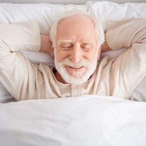 Smiling man with beard resting on his back with a pillow under his head