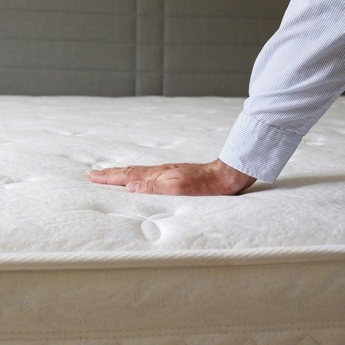 A hand pressing down on the top of a white mattress