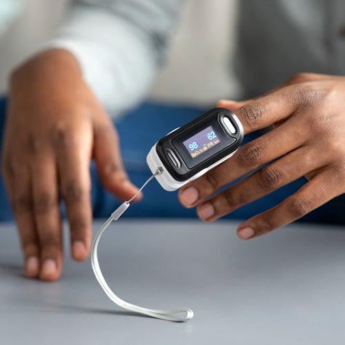 A closeup of a person’s hands with a pulse oximeter on their fingertip