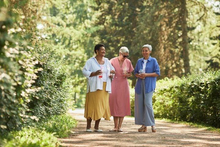 three short-haired older women laughing while walking on a dirt path