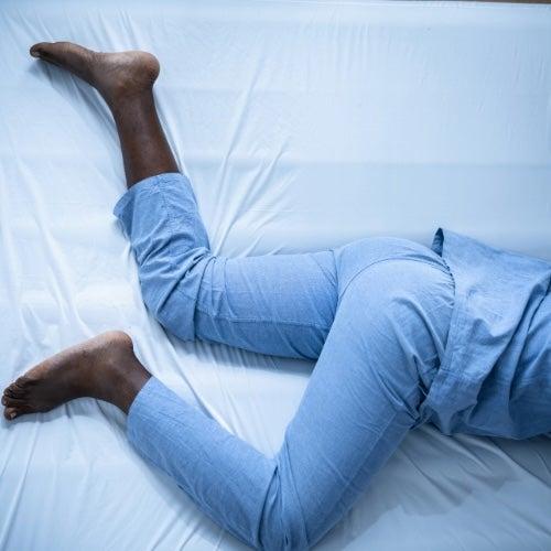 The legs of a person in blue pajamas lying in bed