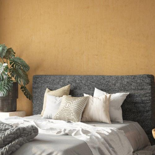 A bedroom with a gray bed, a mustard-colored wall and a large plant.