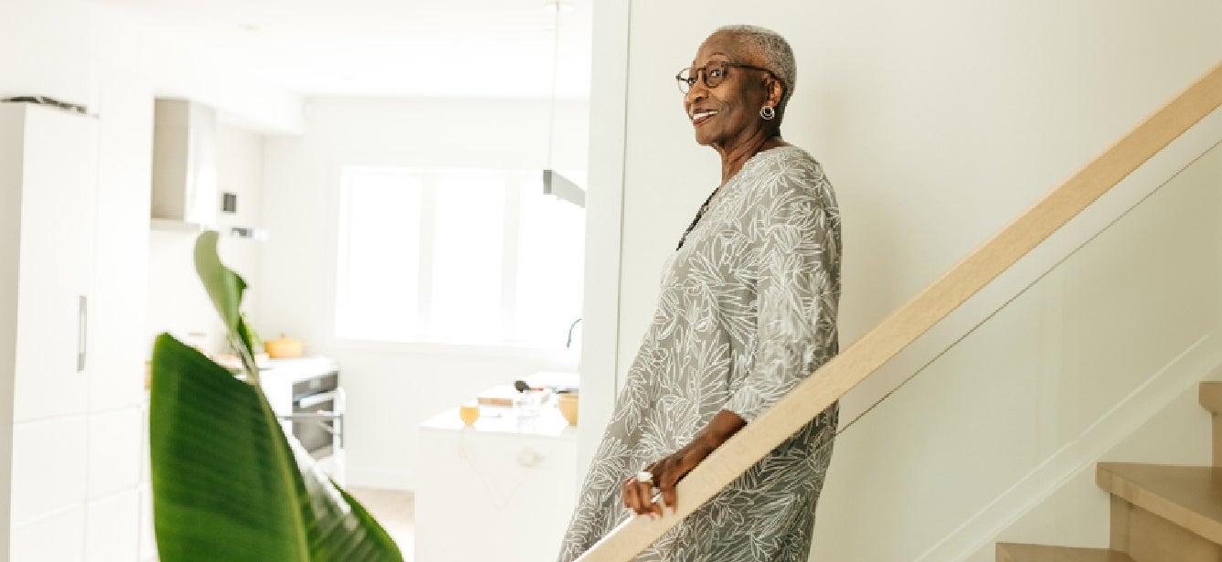 smiling older woman walking down stairs holding handrail