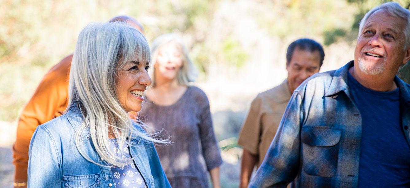 A group of older adults is walking outside, enjoying nature and laughing/smiling.