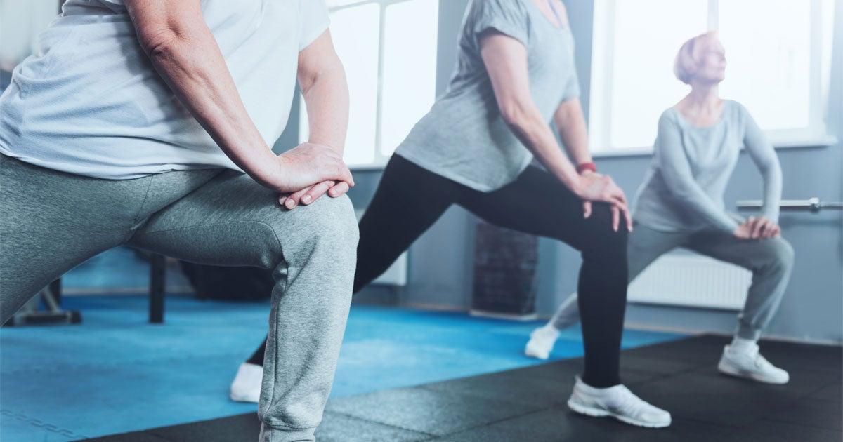 An upclose shot of a group of senior ladies standing in a row and doing lunging exercises while training in a gym.