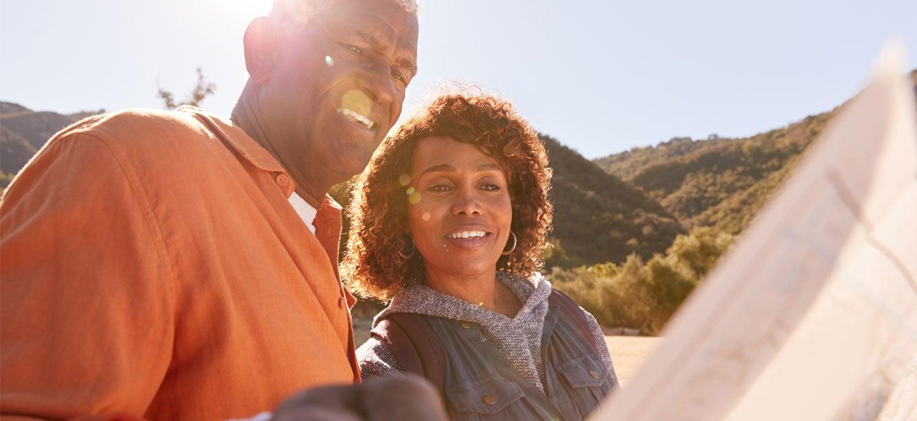 A senior Black man and his daughter are outside enjoying nature, looking at a map.