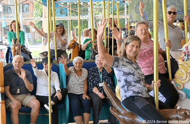 smiling older adults waving from carousel
