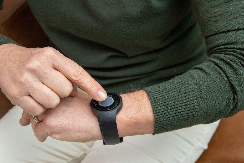 Older woman wears a green sweater and presses the help button on a medical alert watch