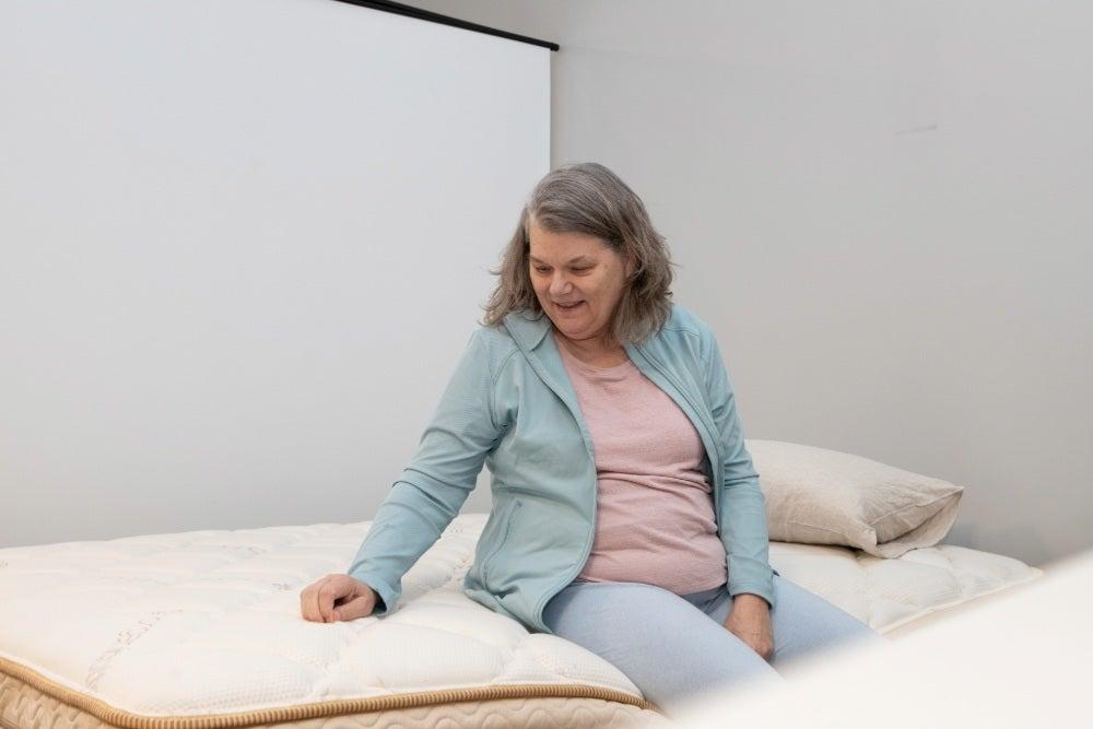 A woman smiles while sitting on the edge of a bed and running her hands over the cover