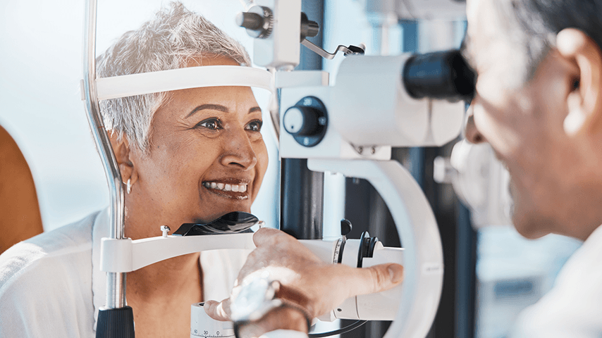 smiling woman with short gray hair getting eye exam from smiling male eye doctor