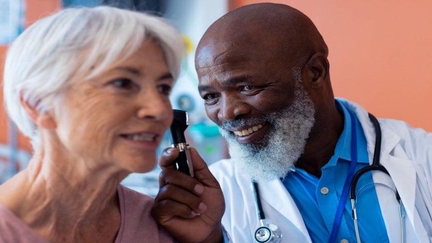 smiling black male doctor examining older white woman's ear