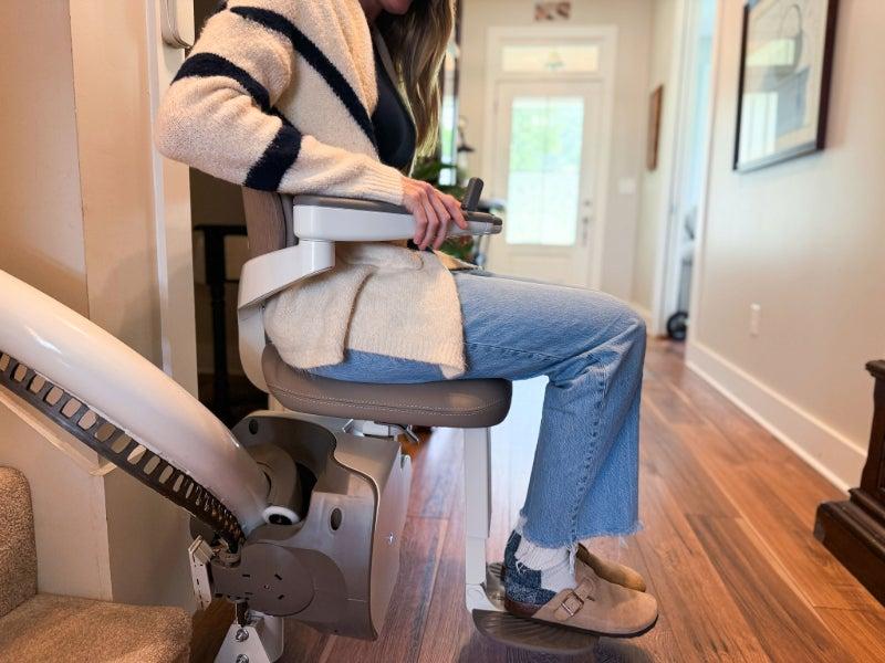Person sits on an Access BDD curved stair lift parked at the bottom of the stairs