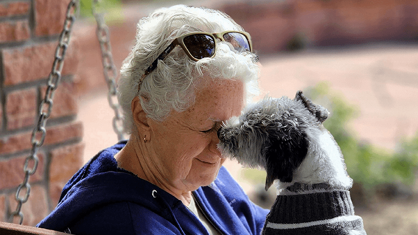 older woman on porch swing getting face kiss from small dog
