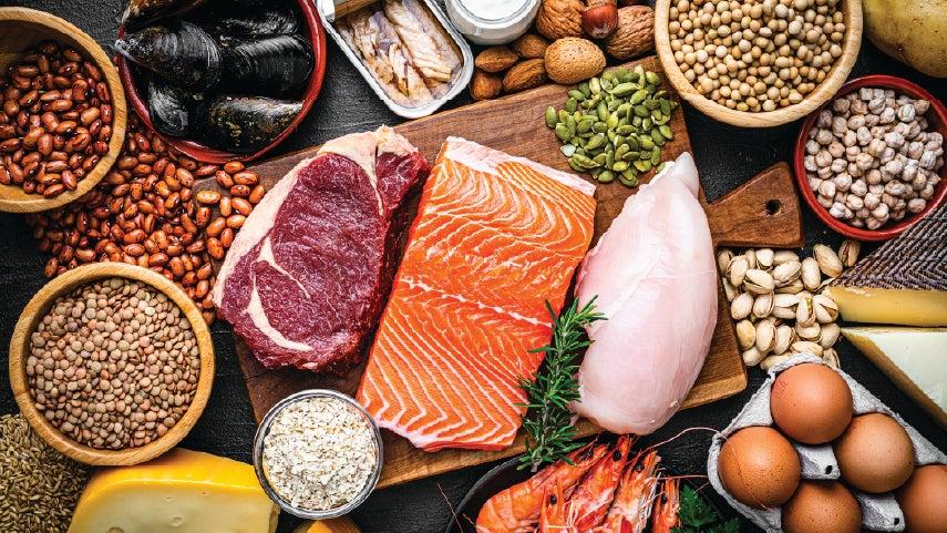 Beautiful, close-up shot of protein-rich food that's on a cutting board, including salmon, steak, chicken, eggs, among others.
