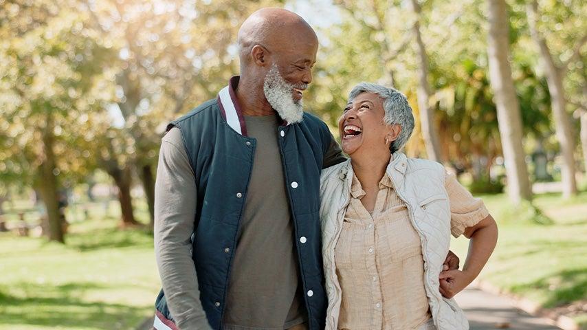 A couple smiling at one another while walking arm-in-arm at a park