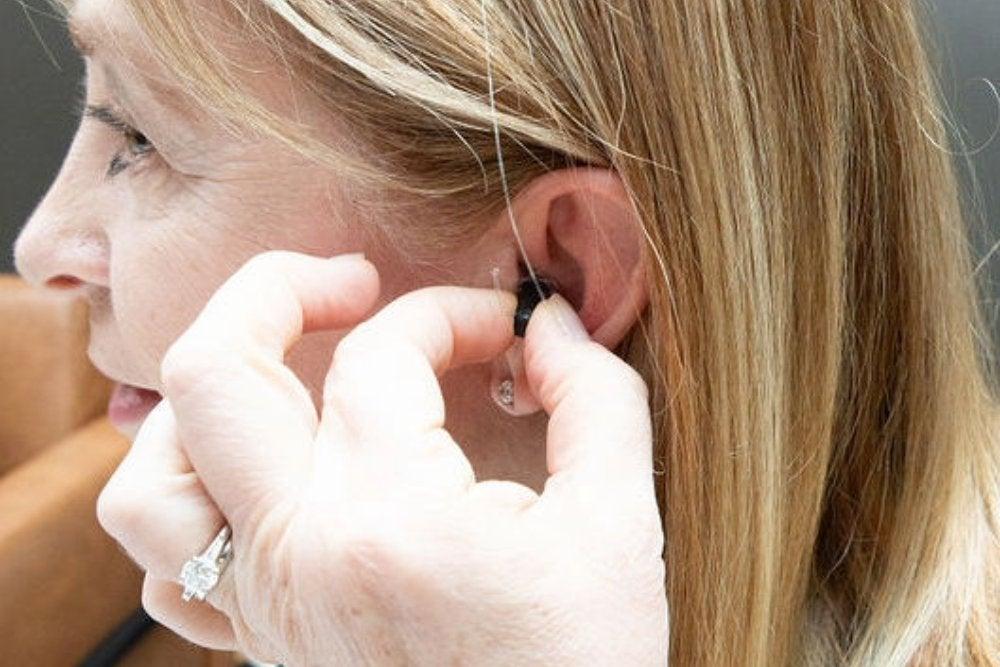 woman placing hearing aid in her left ear