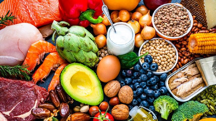 Beautiful, colorful spread of nutritional food on a table, including avocado, walnuts, blueberries, broccoli, and more.