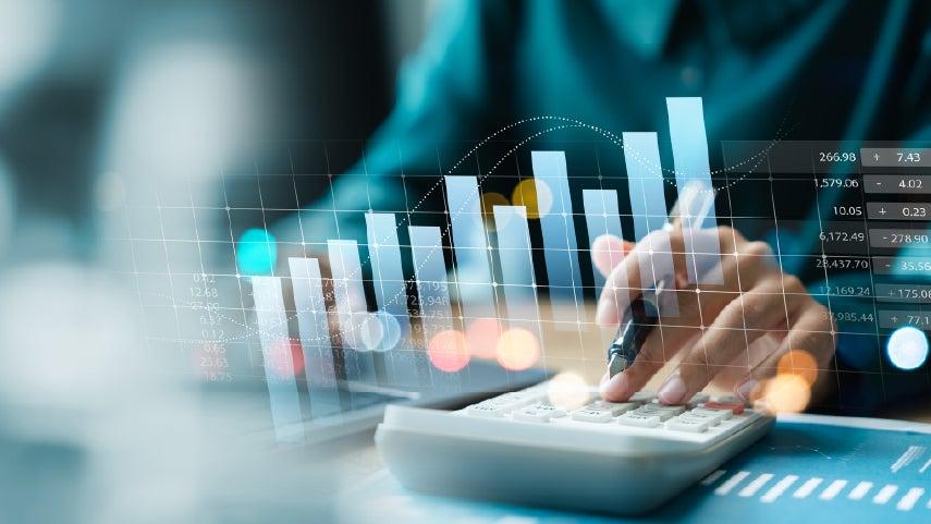 A person is calculating figures with an analog calculator and super imposed on this image are charts/graphs showing growth.