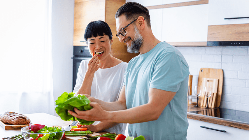 smiling man and woman making salad in brightly lit kitchen