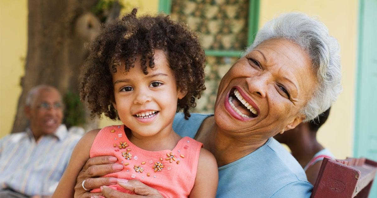 A senior Black woman is holding her granddaughter in her lap during a family get together outside.
