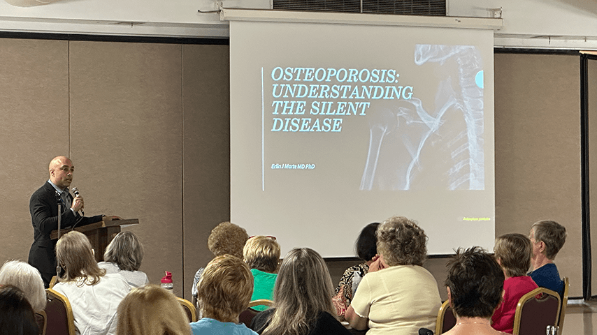 man with microphone in front of screen showing "Osteoporosis: Understanding the Silent Disease"