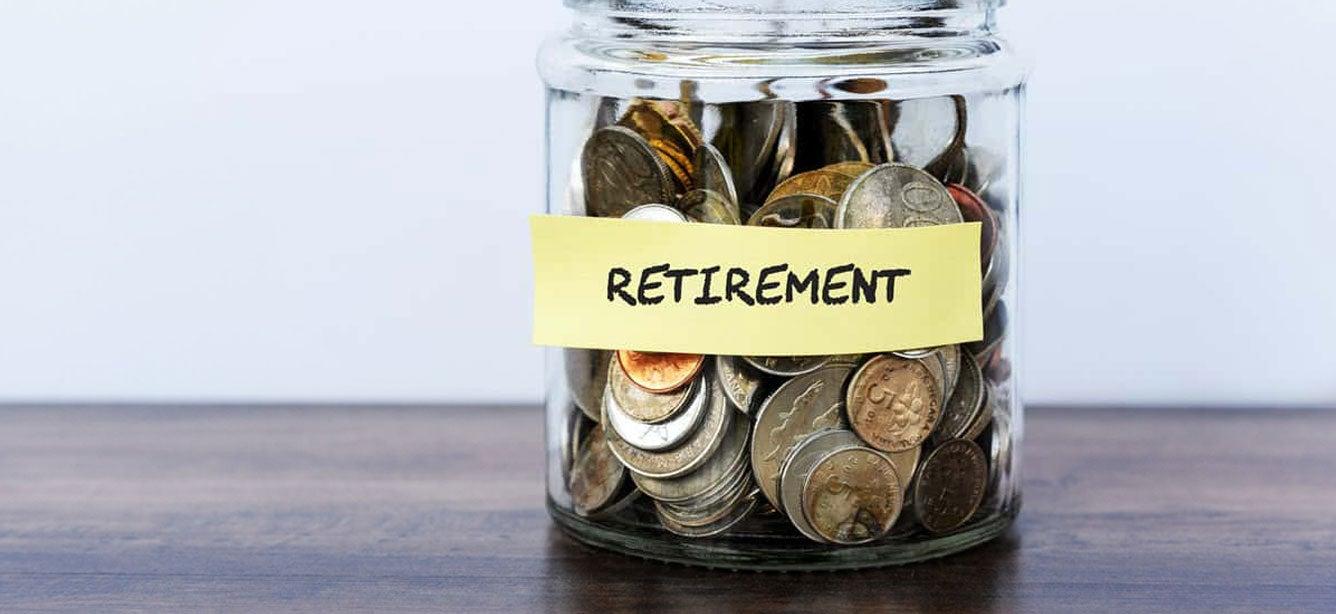 A jar filled with various coins has a sticky note with the words "Retirement" on it.