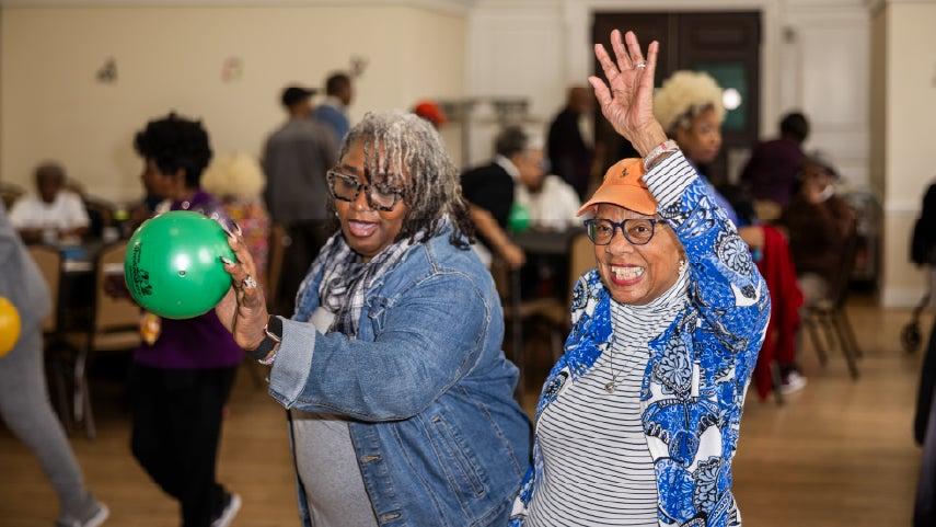 Two women in dancing positions, one holding a balloon.