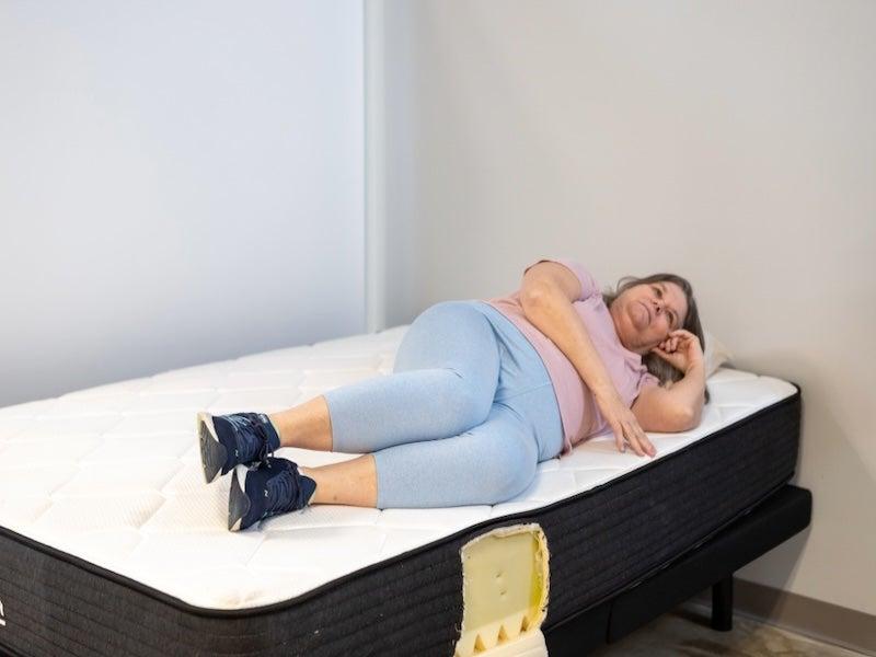 A woman lies on her side near the edge of the Plank Firm mattress