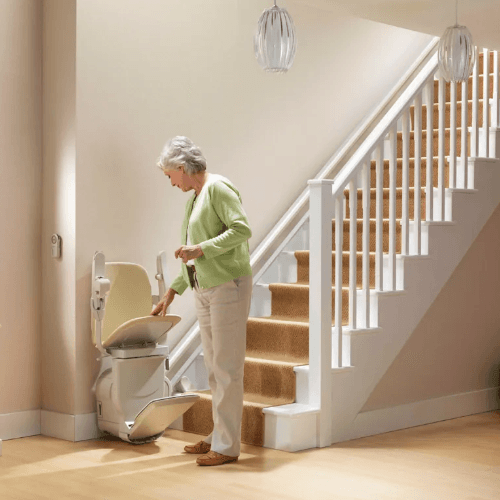 A woman stands at the bottom of the stairs and unfolds her Stannah stair lift