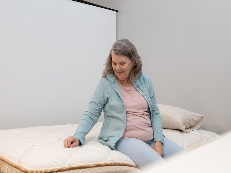 A woman sitting on the edge of the Saatva Solaire adjustable Sleep Number alternative mattress