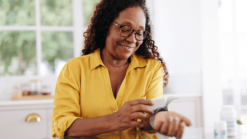 Smiling older black woman checking her blood pressure at home