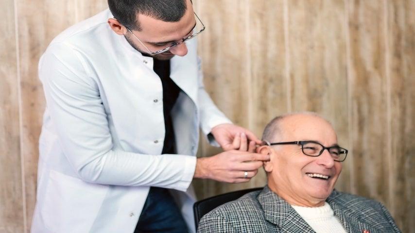 audiologist fitting a smiling older white man with a hearing aid