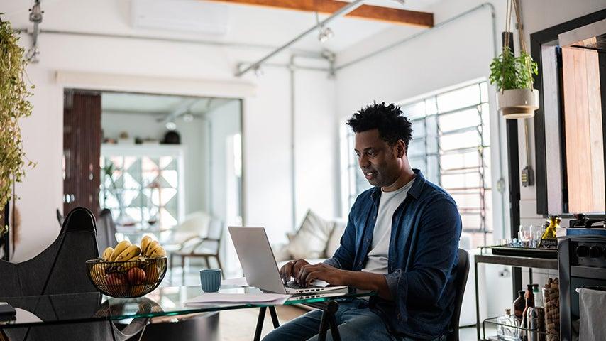 A man sits at a table and types on a computer.