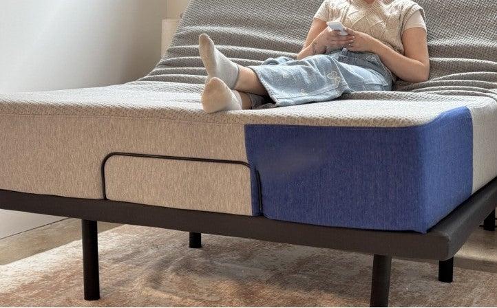 A woman sitting on a mattress on the DreamCloud Adjustable base, holding its remote