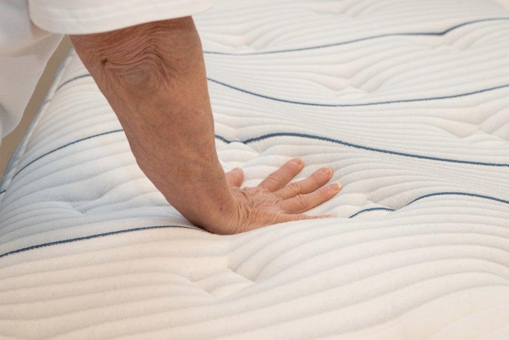 A person pressing their hand down on the top of the Bear Elite Hybrid mattress