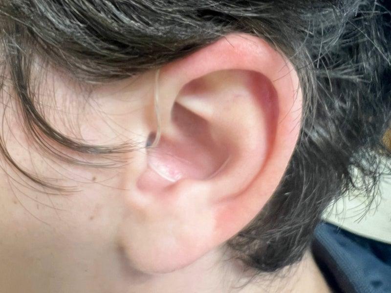 A closeup picture of an ear wearing the Jabra Enhance Select 700 hearing aid, showing only a clear wire