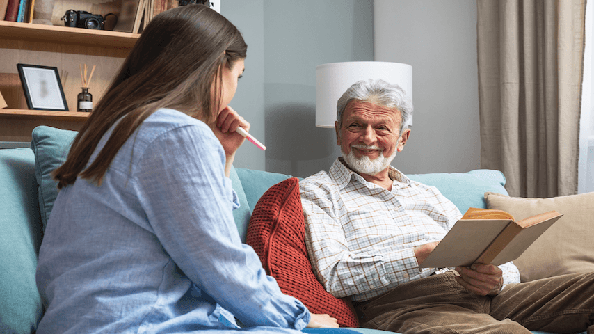 Man holding a book and adult daughter chatting on the couch