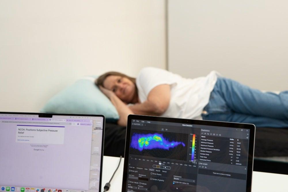 An older adult woman lies on her side on the Nectar Premier Memory Foam mattress while a pressure map shows the support
